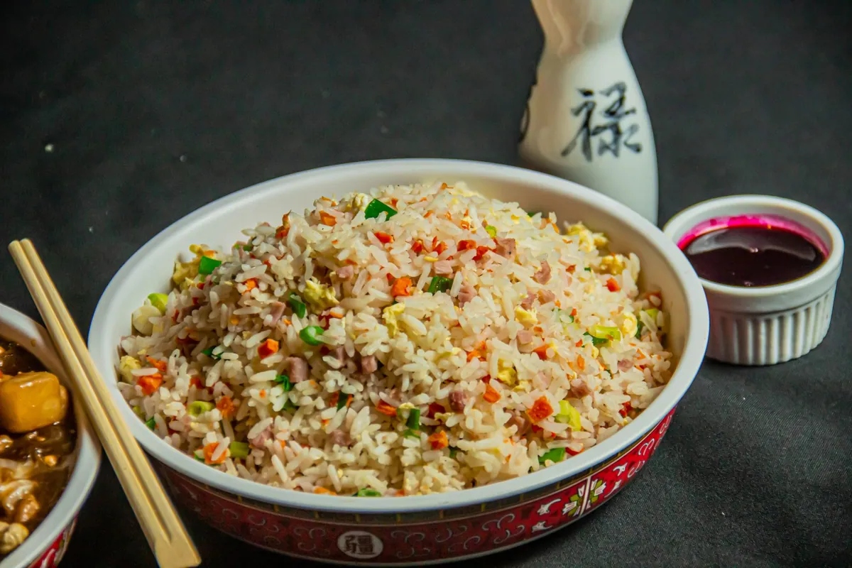 Riz cantonais doré dans un wok, grains de riz séparés et brillants, œufs brouillés, dés de jambon, crevettes roses et petits pois, parsemé d'oignons nouveaux émincés.
